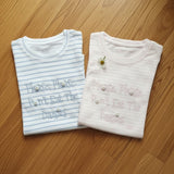 Striped daisy slogan tees in blue and pink folded on a wooden floor