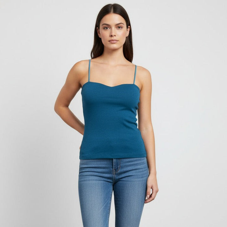 Woman wearing a dark blue tank top and blue jeans against a white background