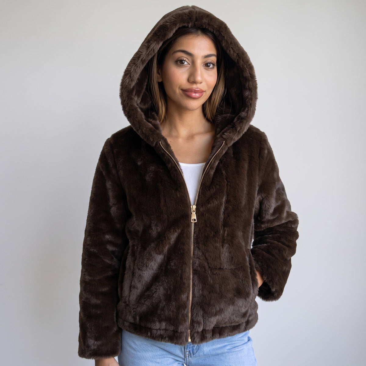 Dark brown faux fur hooded jacket with gold zip worn with the hood up over jeans