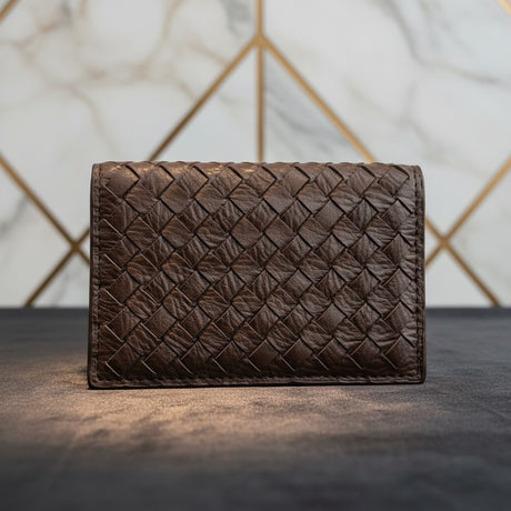 Dark brown woven leather wallet against a patterned wall