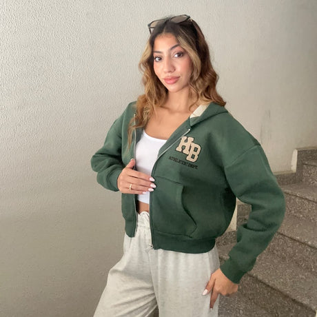 Dark green varsity patch zip hoodie worn half zipped over a white top with grey joggers