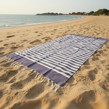 Dark grey thin striped beach towel on sandy beach with ocean view