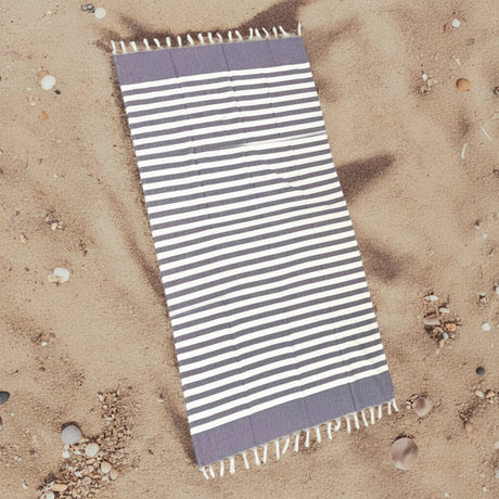 Striped beach towel with purple and white stripes on a sandy background