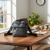 Dark grey crossbody bag on a wooden desk with office items in a bright room