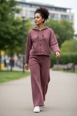 Woman wearing a dark pink casual outfit walking on a sidewalk with greenery in the background