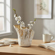 Short gold brushed vase holding white blossom branches on an oak desk by a window