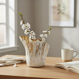 Short gold brushed vase holding white blossom branches on an oak desk by a window