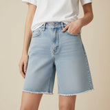 Person wearing denim bermua shorts and a white tshirt on a beige background
