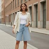 Woman wearing denim bermuda shorts outdoors in front of a brick building