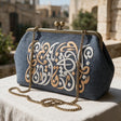 Denim blue frame clutch embroidered with white and gold Arabic letters on a sunny stone terrace