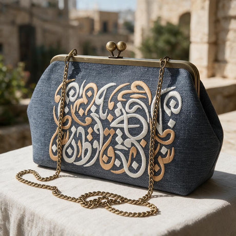 Denim blue frame clutch embroidered with white and gold Arabic letters on a sunny stone terrace