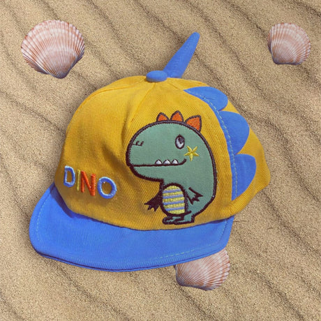 Mustard corduroy cap with blue brim, blue fabric spikes and an embroidered dinosaur, flat on beach sand