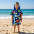 Boy on the beach in a royal blue poncho towel covered in small colourful dinosaurs