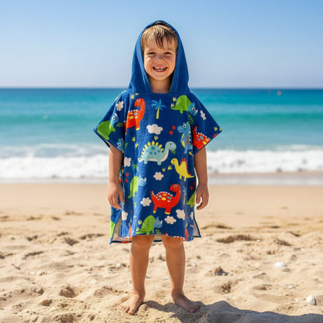 Boy on the beach in a royal blue poncho towel covered in small colourful dinosaurs