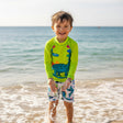 Child wearing a green swimwear and white shorts with dinosaur design at the beach