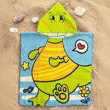 Light blue dino poncho towel with a lime green dinosaur face hood flat lay on sand
