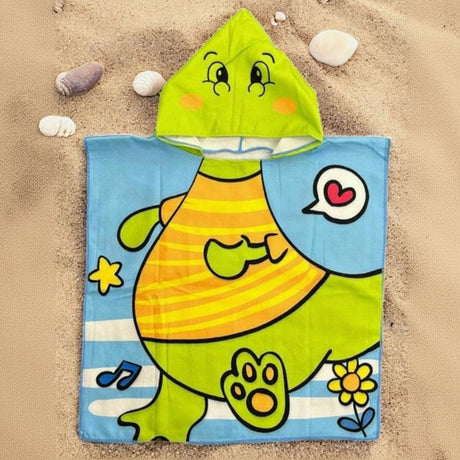 Light blue dino poncho towel with a lime green dinosaur face hood flat lay on sand