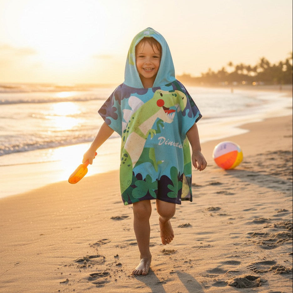 Boy running on the beach in a hooded dinosaur poncho towel with a green T Rex print
