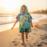 Boy running on the beach in a hooded dinosaur poncho towel with a green T Rex print