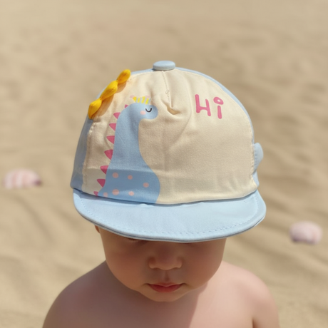 Child on sandy beach in a light blue and cream dinosaur cap with soft yellow spikes along the crown