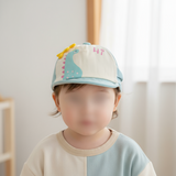 Young child indoors wearing a mint green and cream cap with a turquoise dinosaur and pink Hi lettering