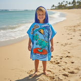 Boy wearing a sky blue poncho towel with a teal dinosaur surfing a wave on a red board