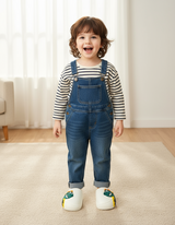 Smiling child in denim dungarees wearing white cosy slippers with a green dinosaur