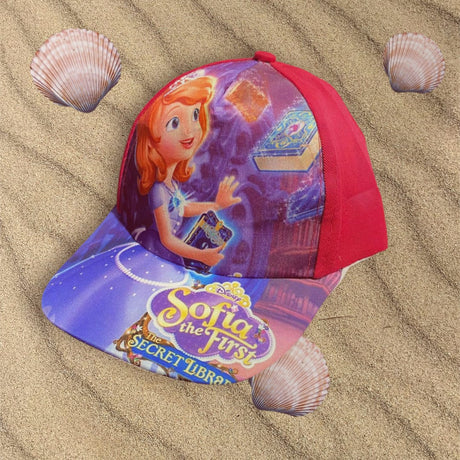 Red and purple girls cap laid flat on sand, printed with a cartoon princess holding a glowing book