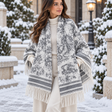 Cream blanket wrap with grey distressed print, striped borders and cream fringe worn in a snowy courtyard
