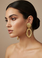Woman wearing gold earrings against a beige background