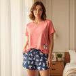 Woman wearing a pink t-shirt and blue shorts with dog pattern in a bedroom setting
