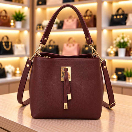 Burgundy pebbled bucket bag with a gold rectangle clasp, double tab tassels and a crossbody strap