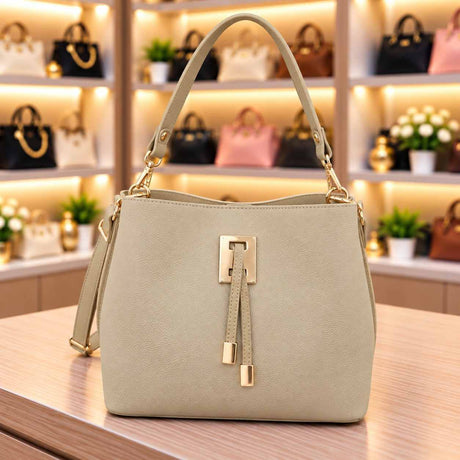 Pale cream bucket bag with a matching top handle, gold clasp and double tab front on a counter