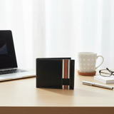 Black wallet with striped design on a desk next to a laptop, mug, and glasses