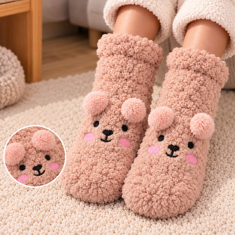 Dusty pink fuzzy kids socks with an embroidered bear face and soft pom pom ears on a cream rug