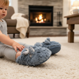 Toddler reaching for soft blue grey fluffy slippers with checked bows by a fireplace