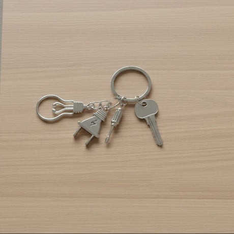 Electrician keychain with light bulb, plug, and screwdriver charms on light wood