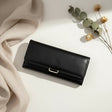 Black leather wallet on a light surface with beige fabric and dried flowers