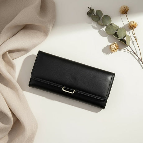Black leather wallet on a light surface with beige fabric and dried flowers