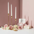 Three gold holders with white tapers among roses, ranunculus and a ribboned box