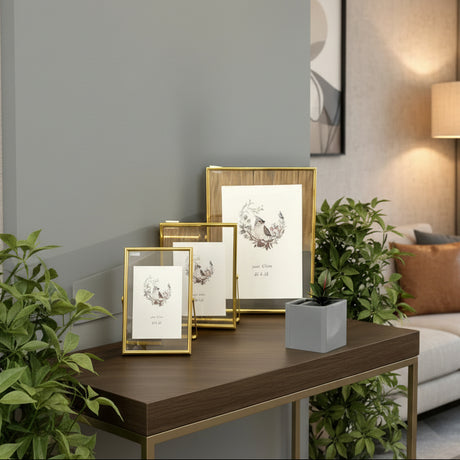 Three slim gold edged frames staggered by size on a dark console among green foliage