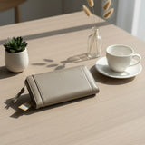 Grey wallet on a wooden table with a cup, a vase, and a plant