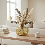 Olive tinted glass vase of dried pampas and eucalyptus on a coffee table by a window