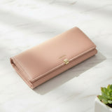 Pink wallet on a light surface with a plant in the corner