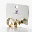Gold earring set on a card with a green crystal hoop, a ball charm huggie and two green teardrop studs