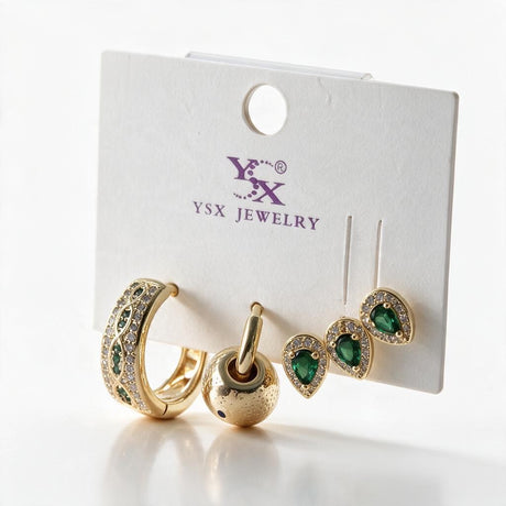 Gold earring set on a card with a green crystal hoop, a ball charm huggie and two green teardrop studs