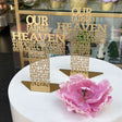 Two gold English prayer crosses on a shop plinth beside a large pink peony