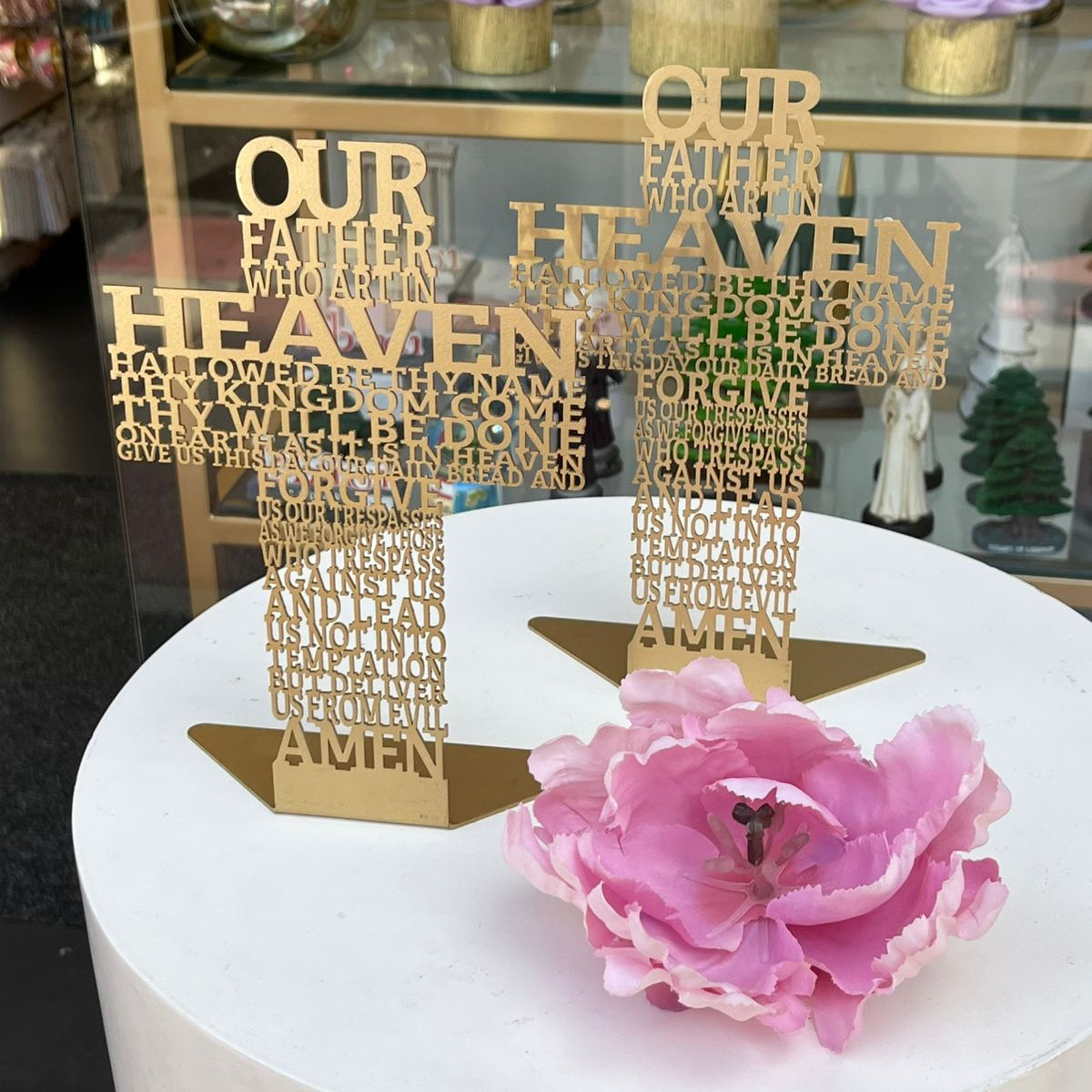 Two gold English prayer crosses on a shop plinth beside a large pink peony