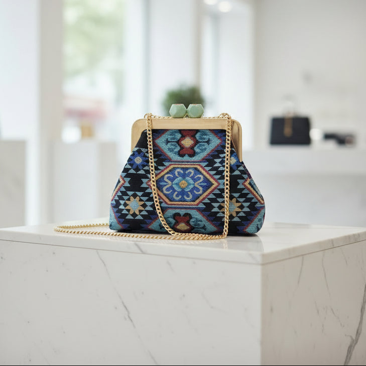 Blue embroidered frame bag on a marble block with its long gold chain