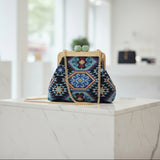 Blue embroidered frame bag on a marble block with its long gold chain